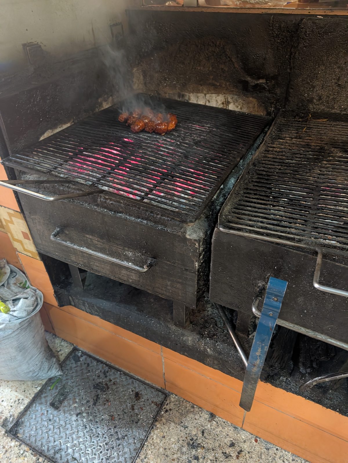 Chorizo cooking over glowing charcoal at Pasillo de Humo