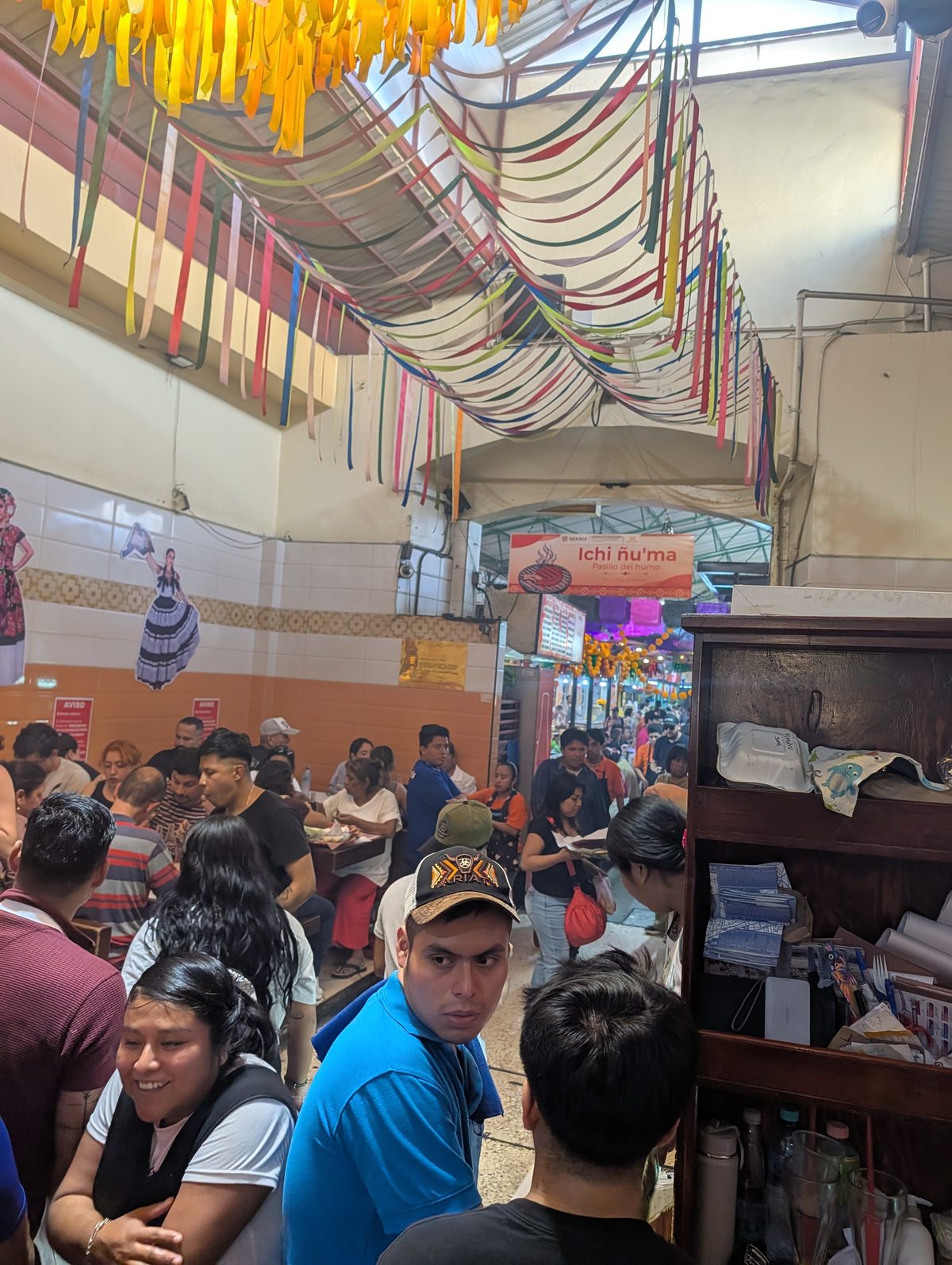 Crowded communal dining area inside Mercado 20 de Noviembre in Oaxaca under colorful papel picado streamers