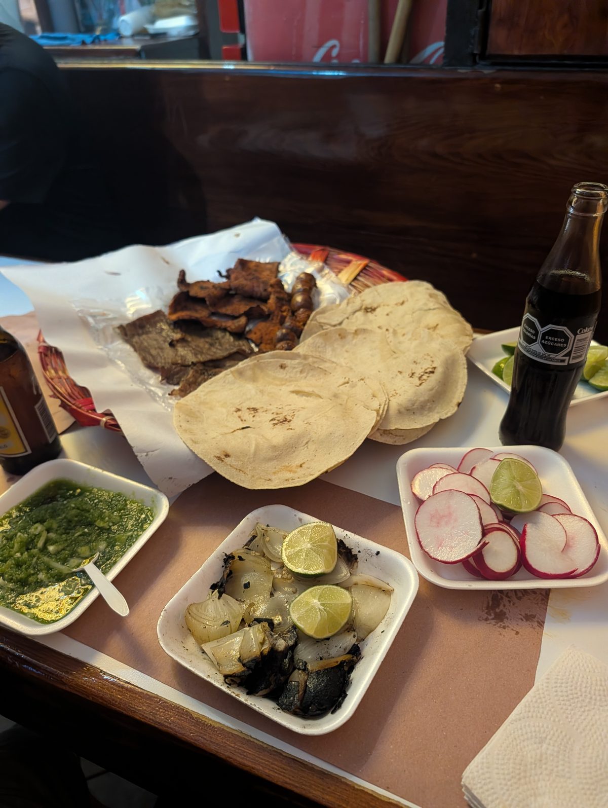 Grilled meat, tortillas, salsa verde, limes, radishes and grilled onions on the table at Pasillo de Humo